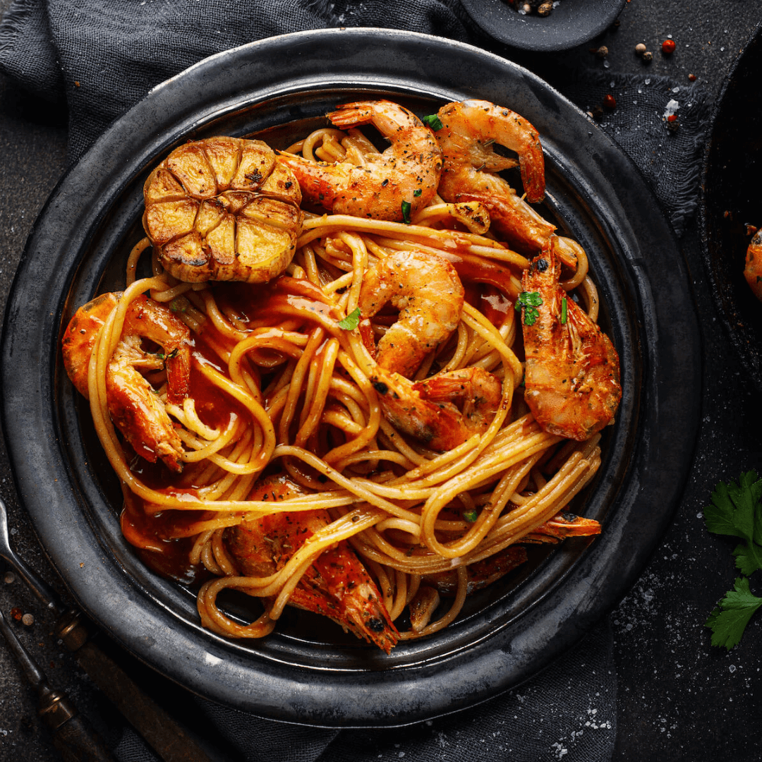 Pasta mit Shrimps und karamellisierter Knoblauchknolle in Tomatensoße auf einem Teller